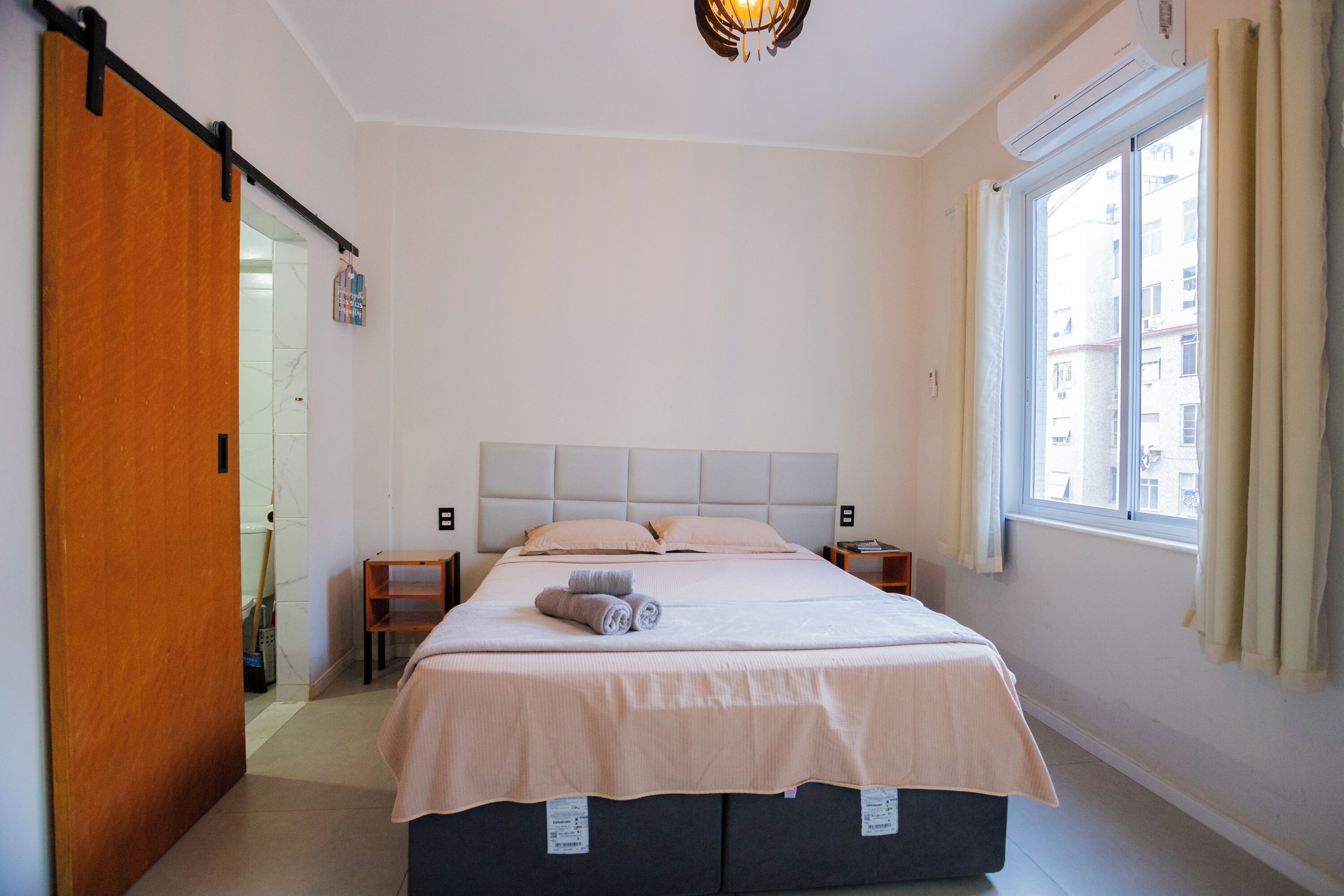 A bedroom with a bed, a nightstand, a window with curtains, and a door.