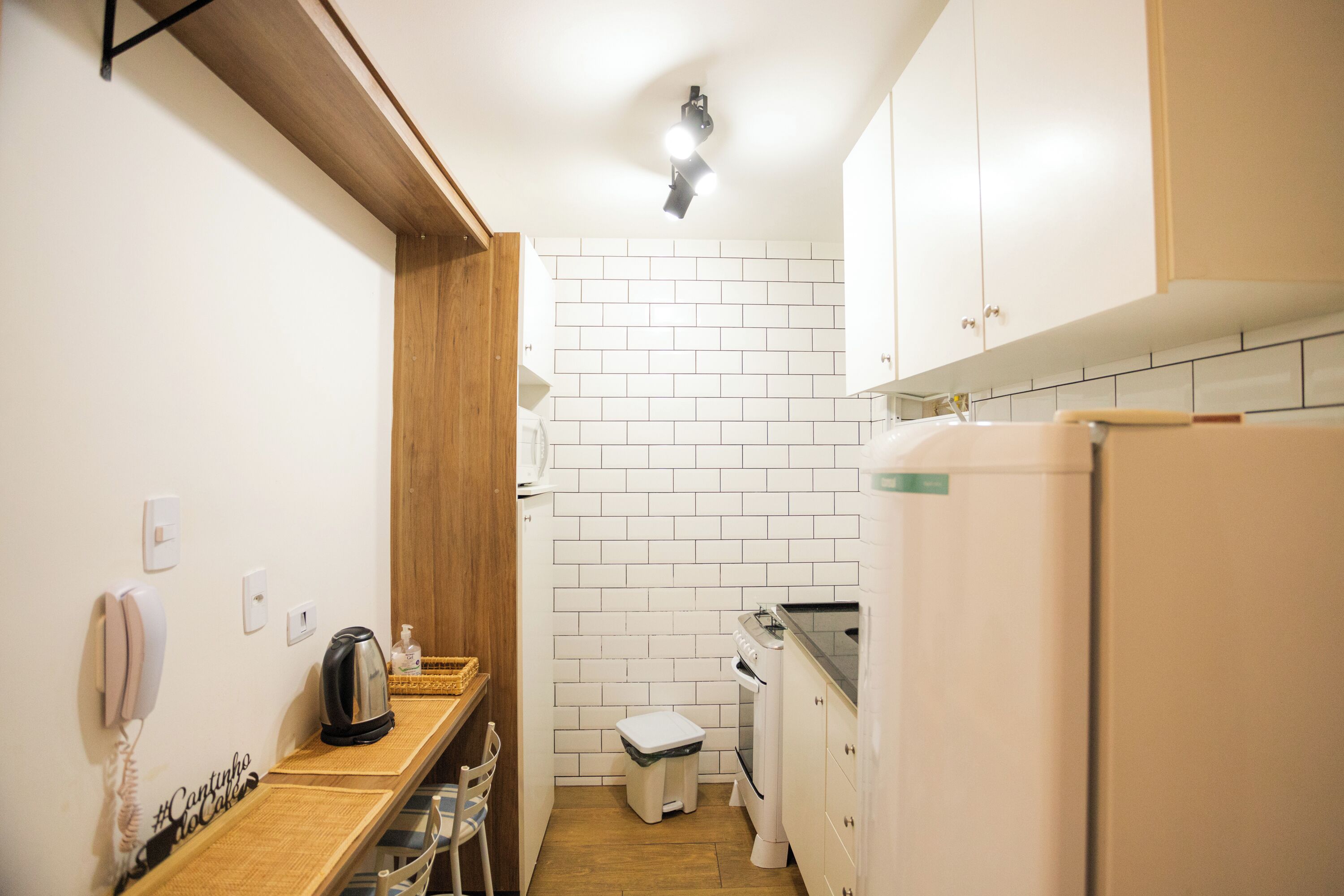 Una cocina compacta con armarios blancos, encimera de madera, hervidor, tostadora y un pequeño cubo de basura.