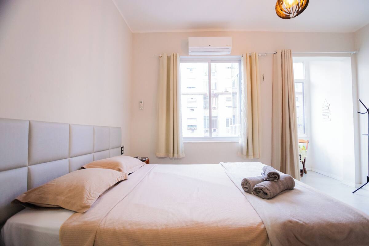 Una habitación de hotel con una cama grande, cabecera, ventana con cortinas y ventilador de techo.