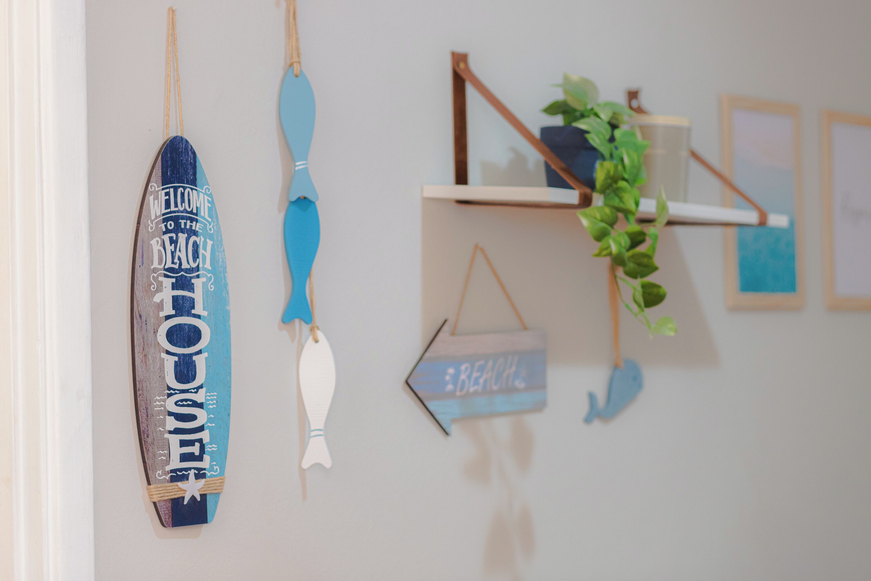 Pared decorada con varios elementos, incluyendo una tabla de surf, un pez y un cartel que dice 'Welcome to the Beach'.