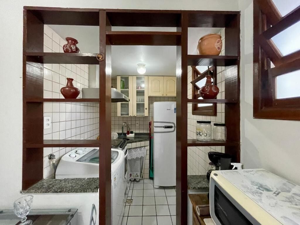 A kitchen with a white refrigerator, a microwave, and a sink. There are shelves with decorative items and a window with a view of the outside.
