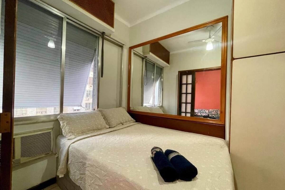 Un dormitorio con cama, un espejo grande y una ventana con persianas.