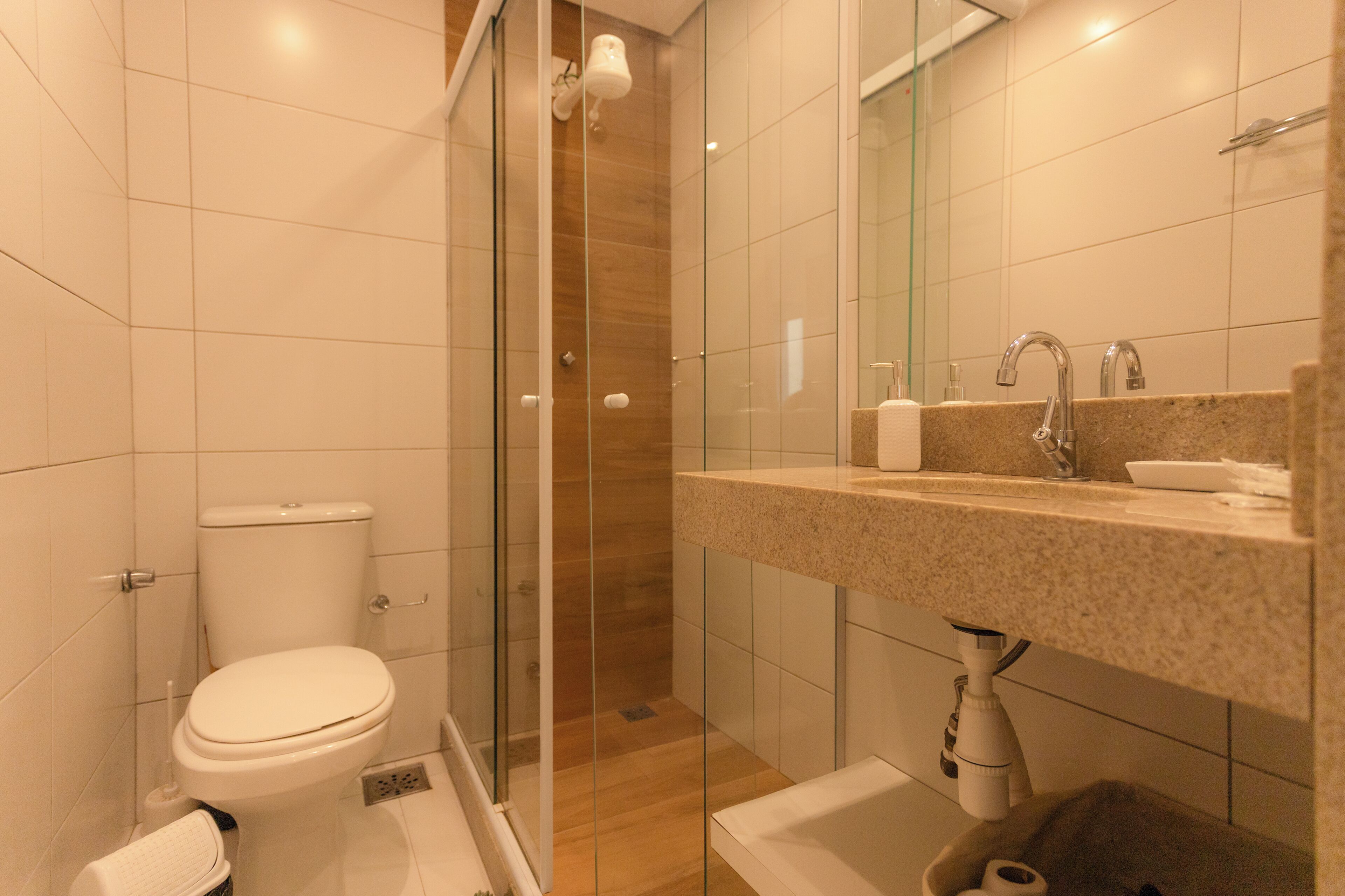 Une salle de bain moderne dotée d’une douche à parois de verre, de toilettes, d’un lavabo avec un plan de travail en granit et d’un miroir au-dessus du lavabo.