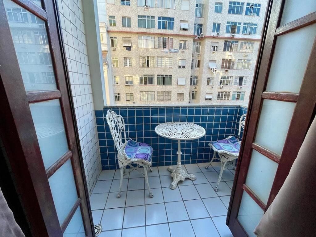 Ein Balkon mit zwei weißen Metallstühlen und einem kleinen runden Tisch, mit Blick auf ein Wohngebäude.