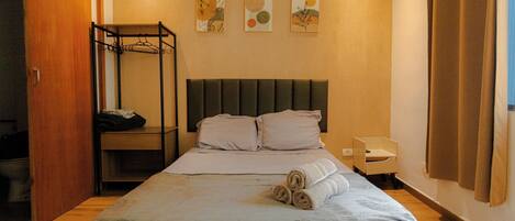 A neatly made bed with a headboard, a wooden wardrobe, and a small bedside table with a lamp.