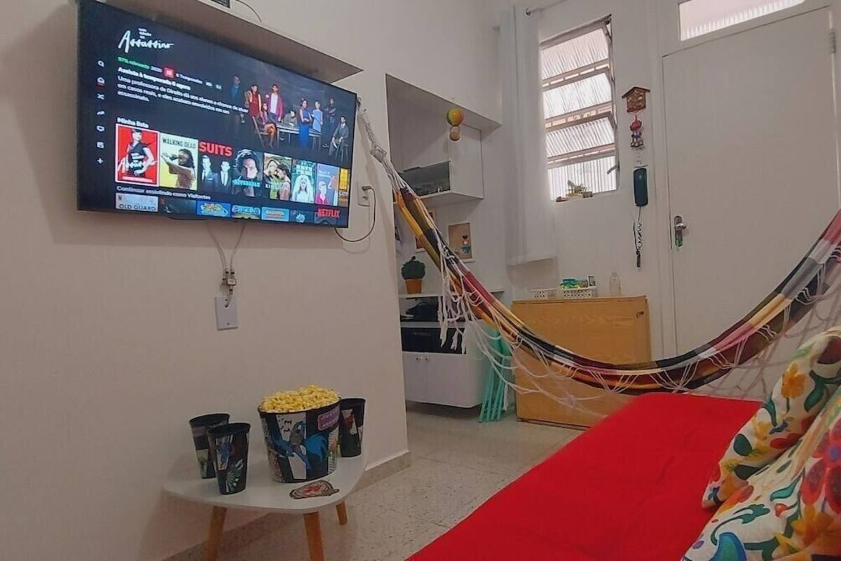 Una habitación con una televisión montada en la pared mostrando la interfaz de un servicio de streaming, una hamaca, un sofá rojo y una mesita con botes de palomitas de maíz.