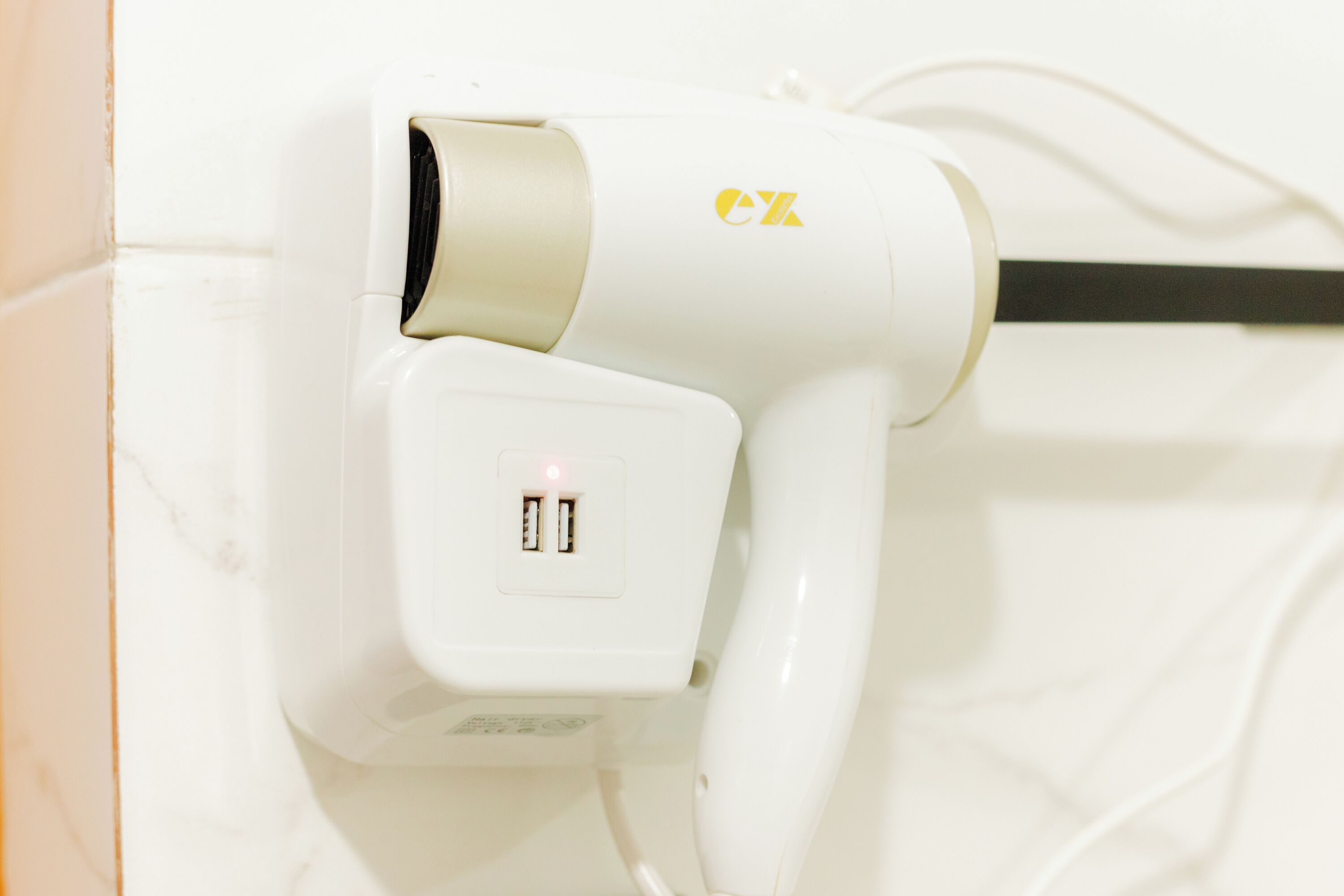 A white hair dryer with a USB port and a power cord plugged in.