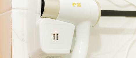 A white hair dryer with a USB port and a power cord plugged in.