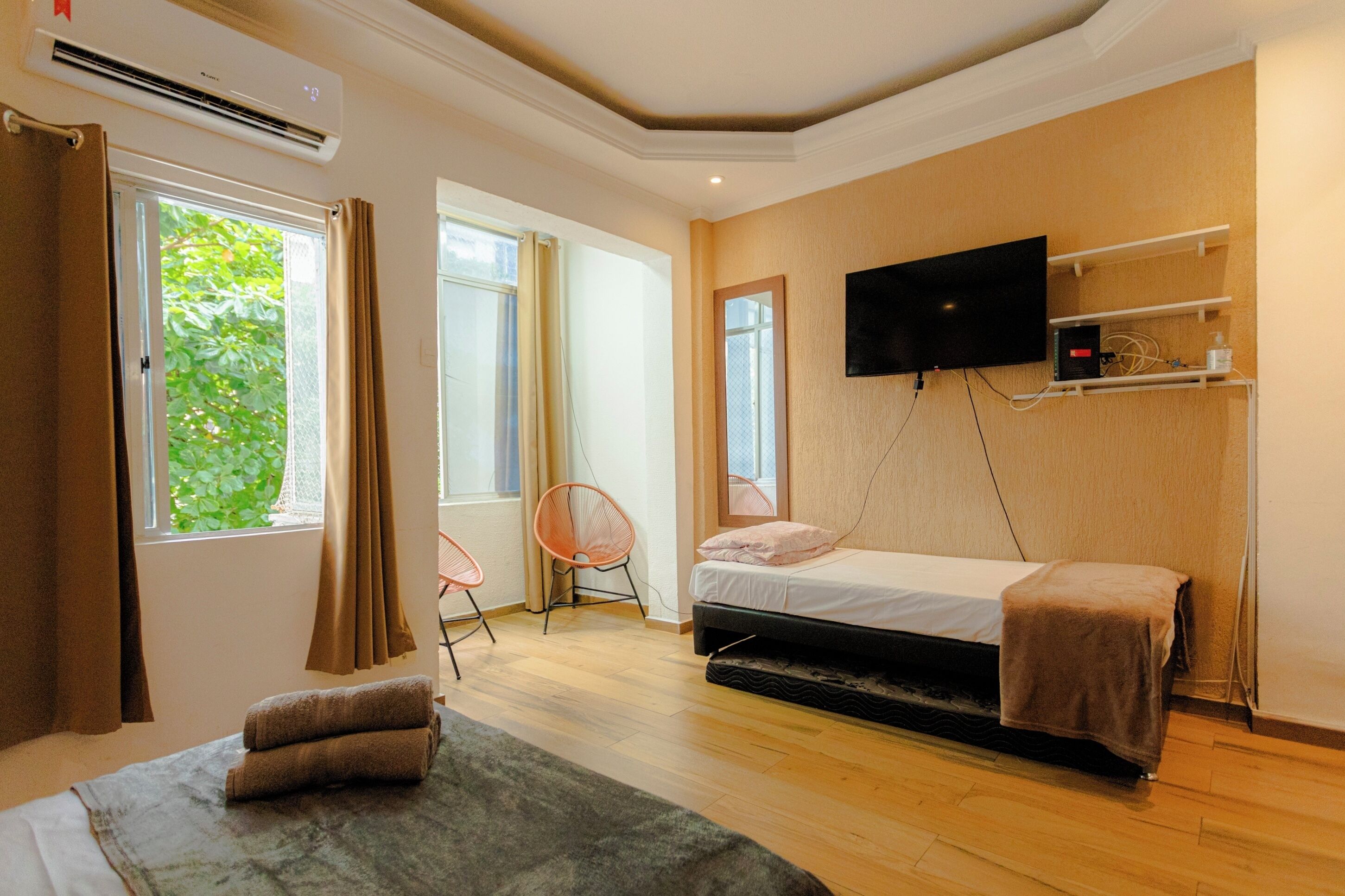 Ein Schlafzimmer mit einem Bett, einem an der Wand montierten Fernseher und einem Fenster mit Vorhängen.