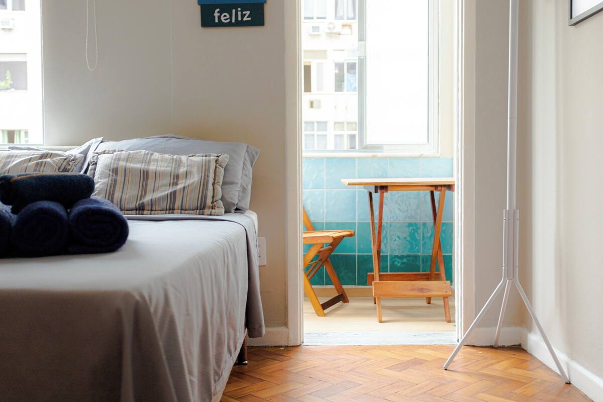 Una habitación de hotel con una cama, una mesita pequeña y un trípode.
