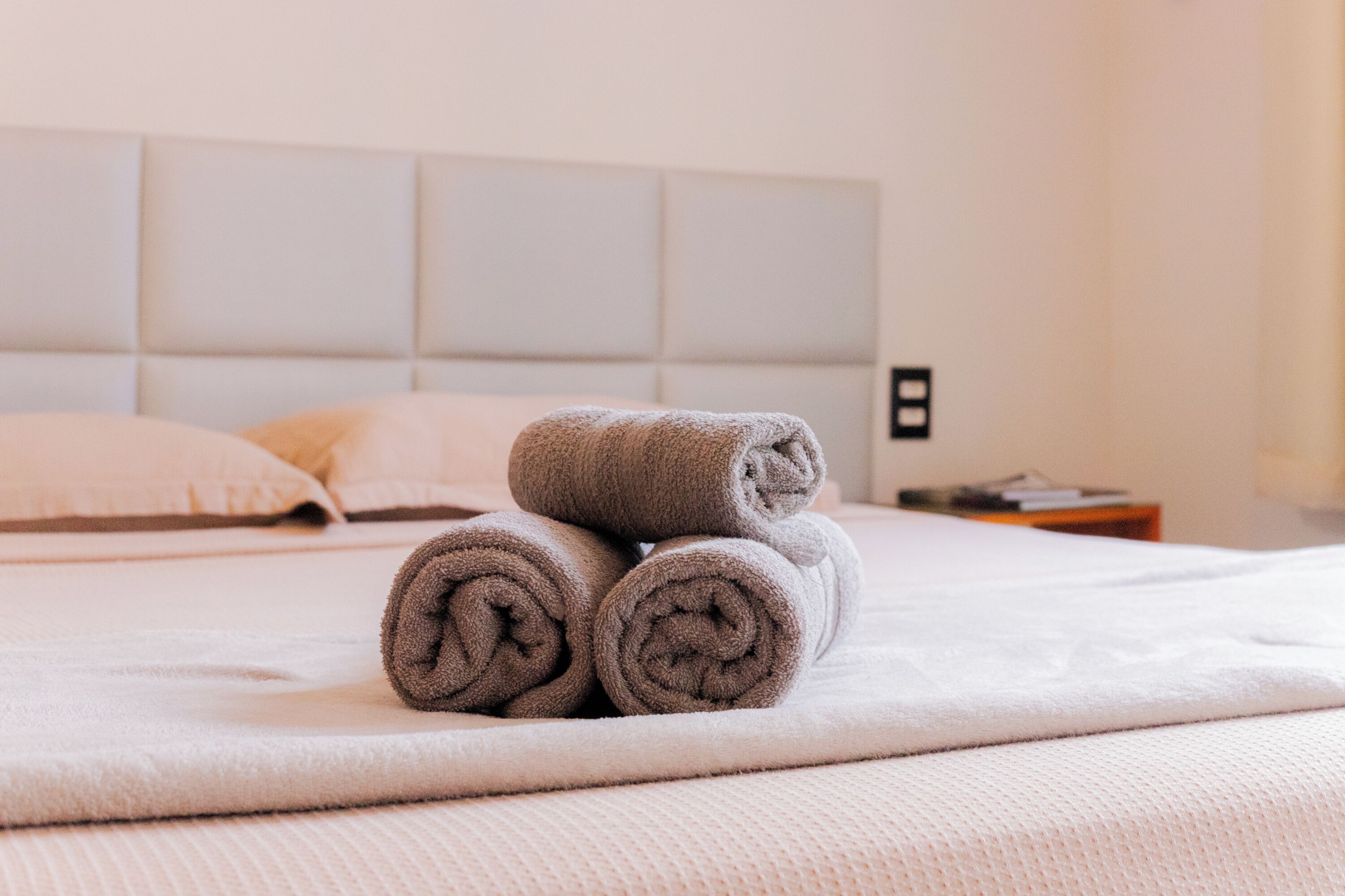 A neatly made bed with rolled towels and a headboard.