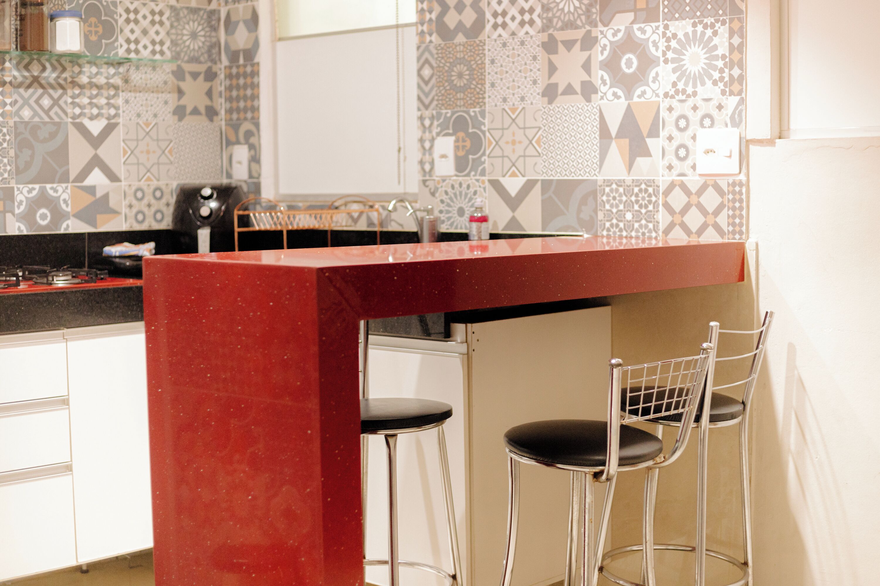 Een keuken met een rode aanrecht, twee barkrukken en een decoratieve spatwand.