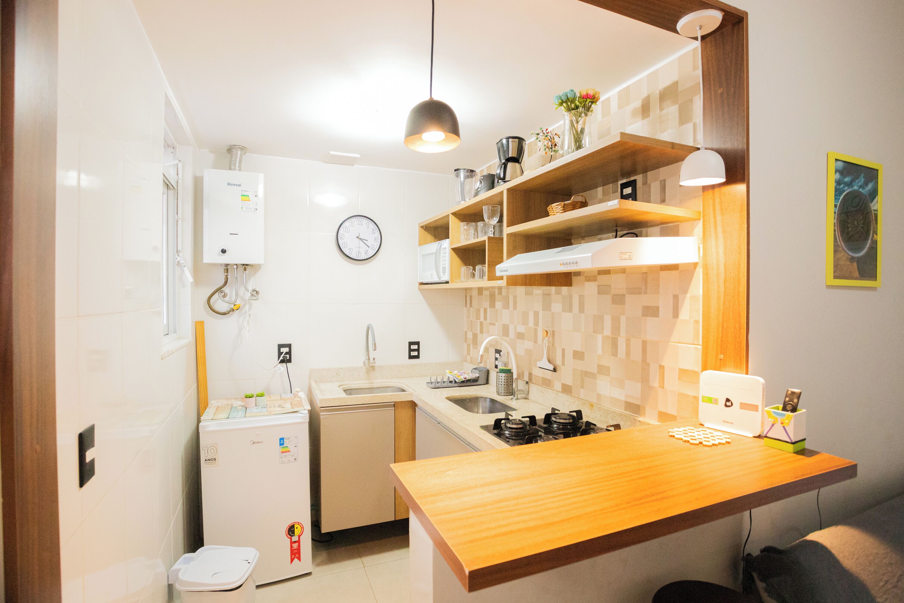 Cocina compacta con lavavajillas integrado, estufa y fregadero. Hay un reloj en la pared y un refrigerador pequeño.
