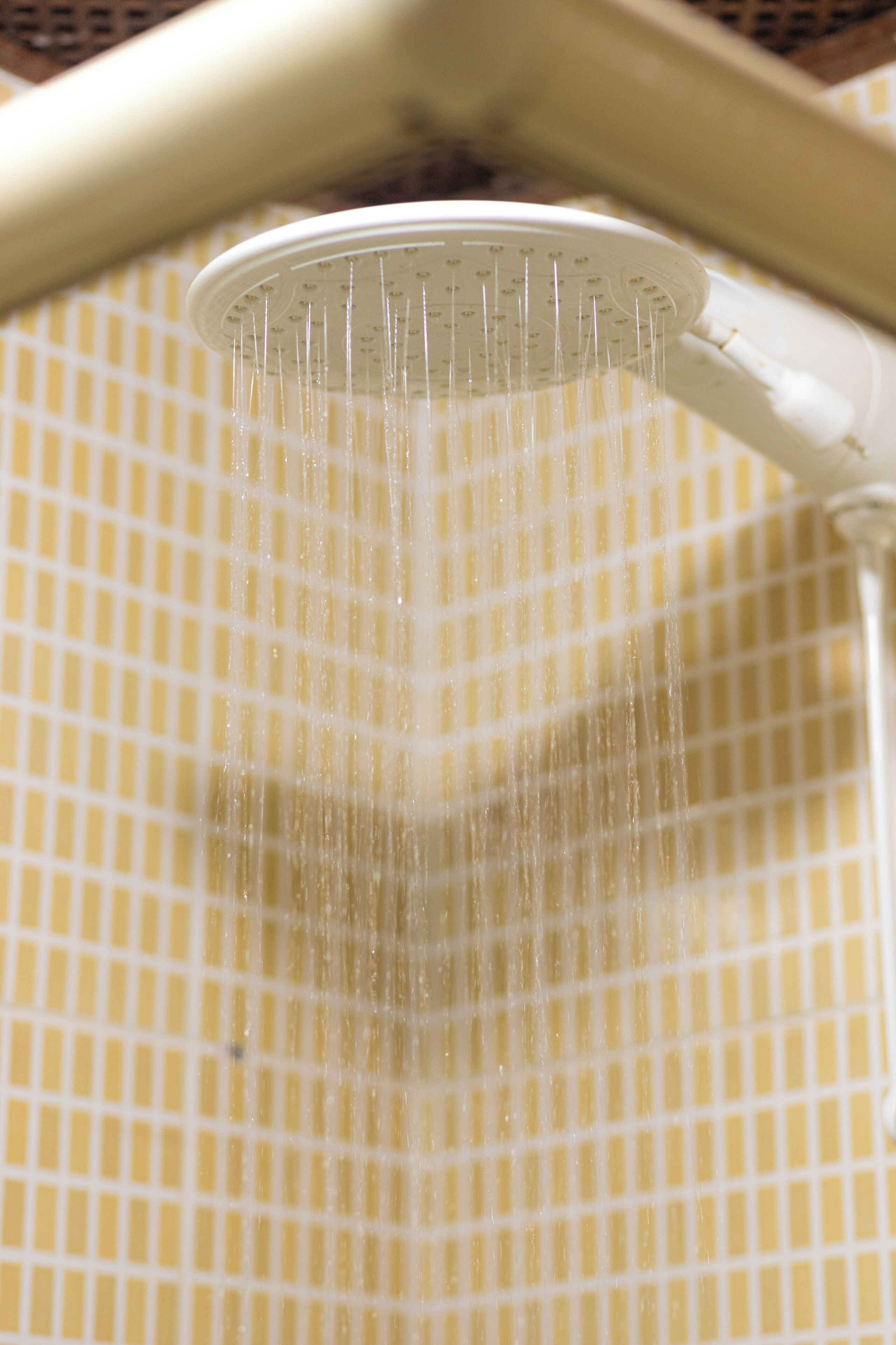 A showerhead with water flowing down a tiled wall.
