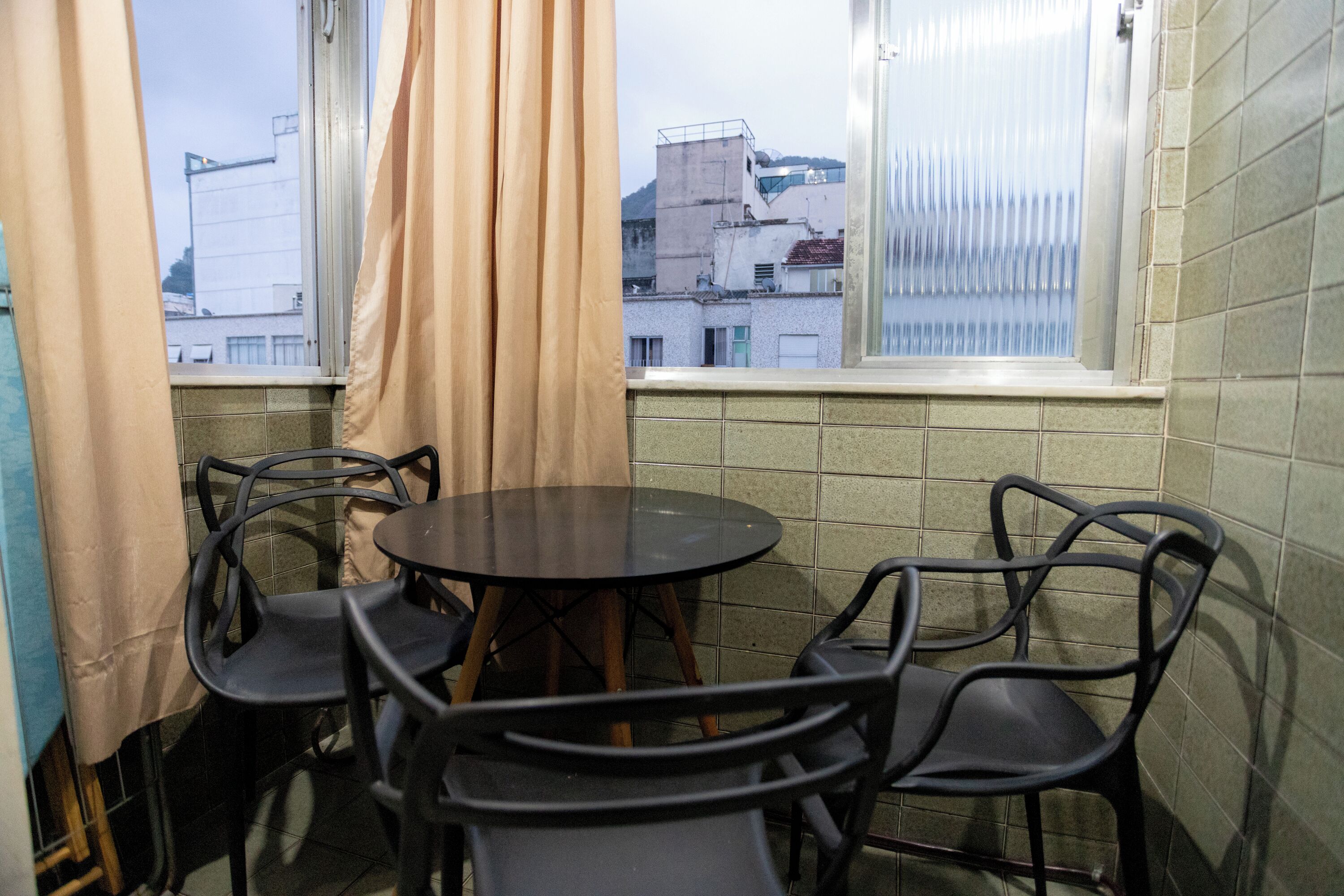 A small room with a round table and four chairs, a window with curtains, and tiled walls.