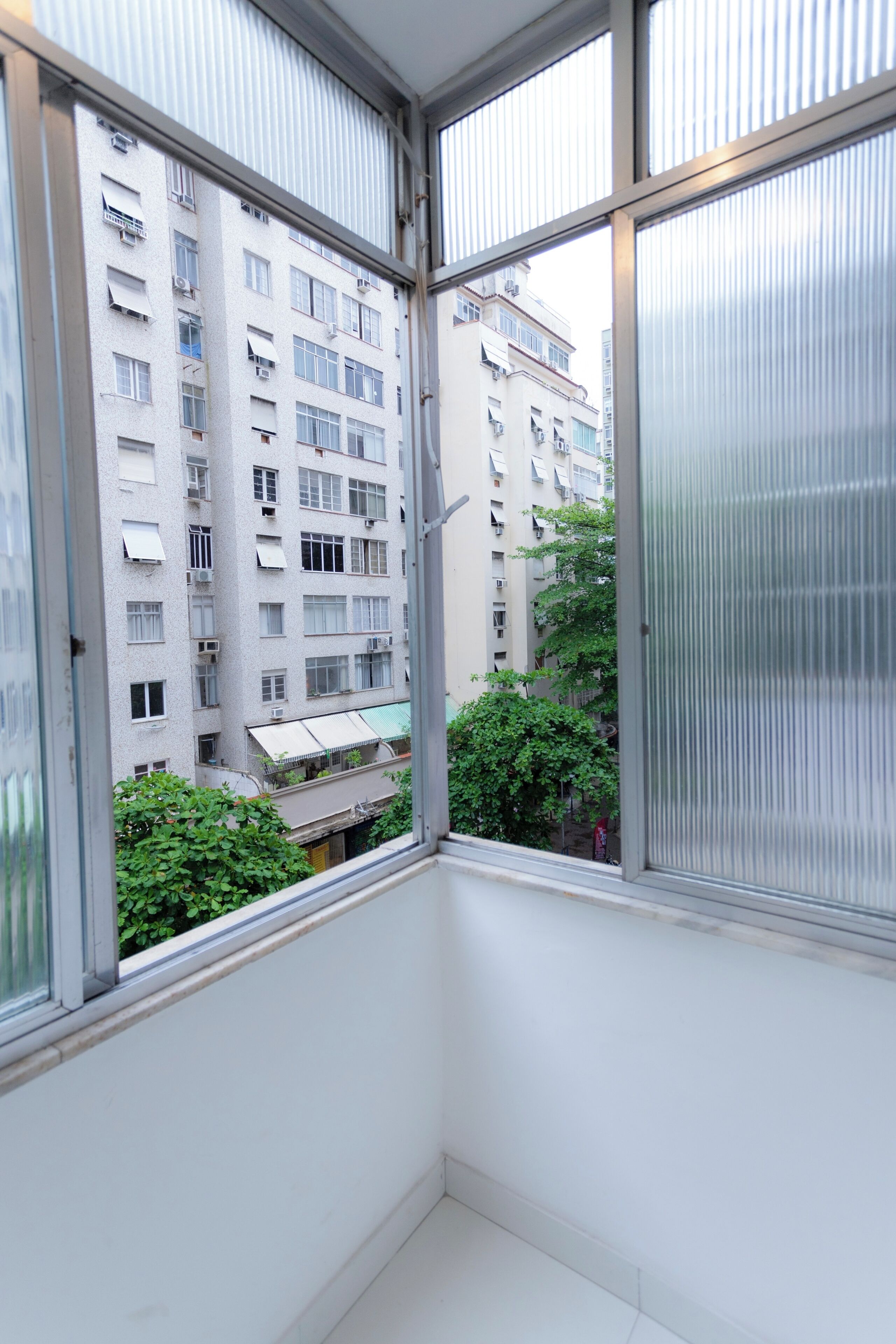 A corner of a room with a view of a multi-story building with balconies and air conditioning units.