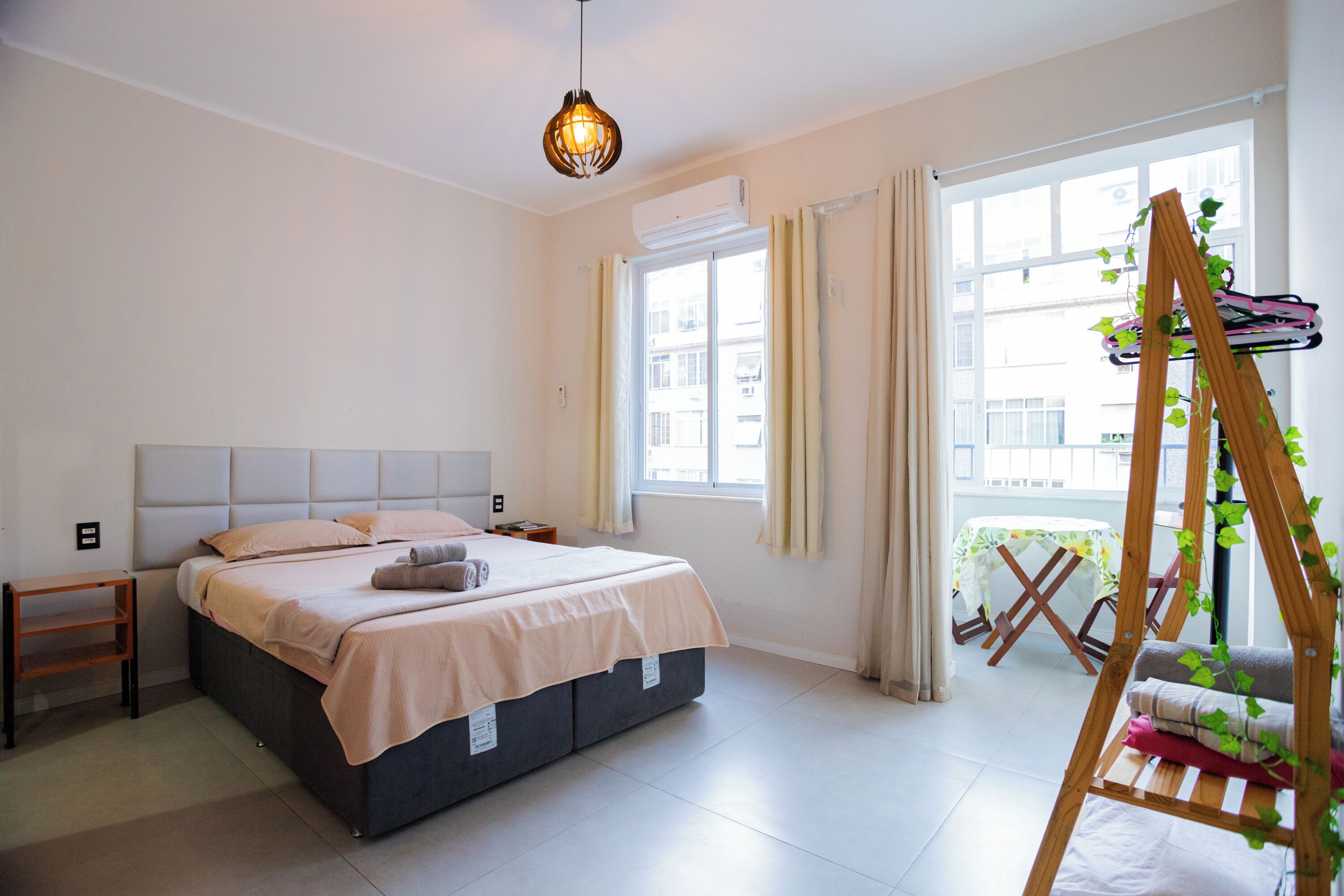 Un dormitorio con cama, mesita de noche, planta colgante y una ventana con cortinas.