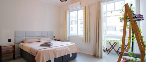 A bedroom with a bed, bedside table, hanging plant, and a window with curtains.
