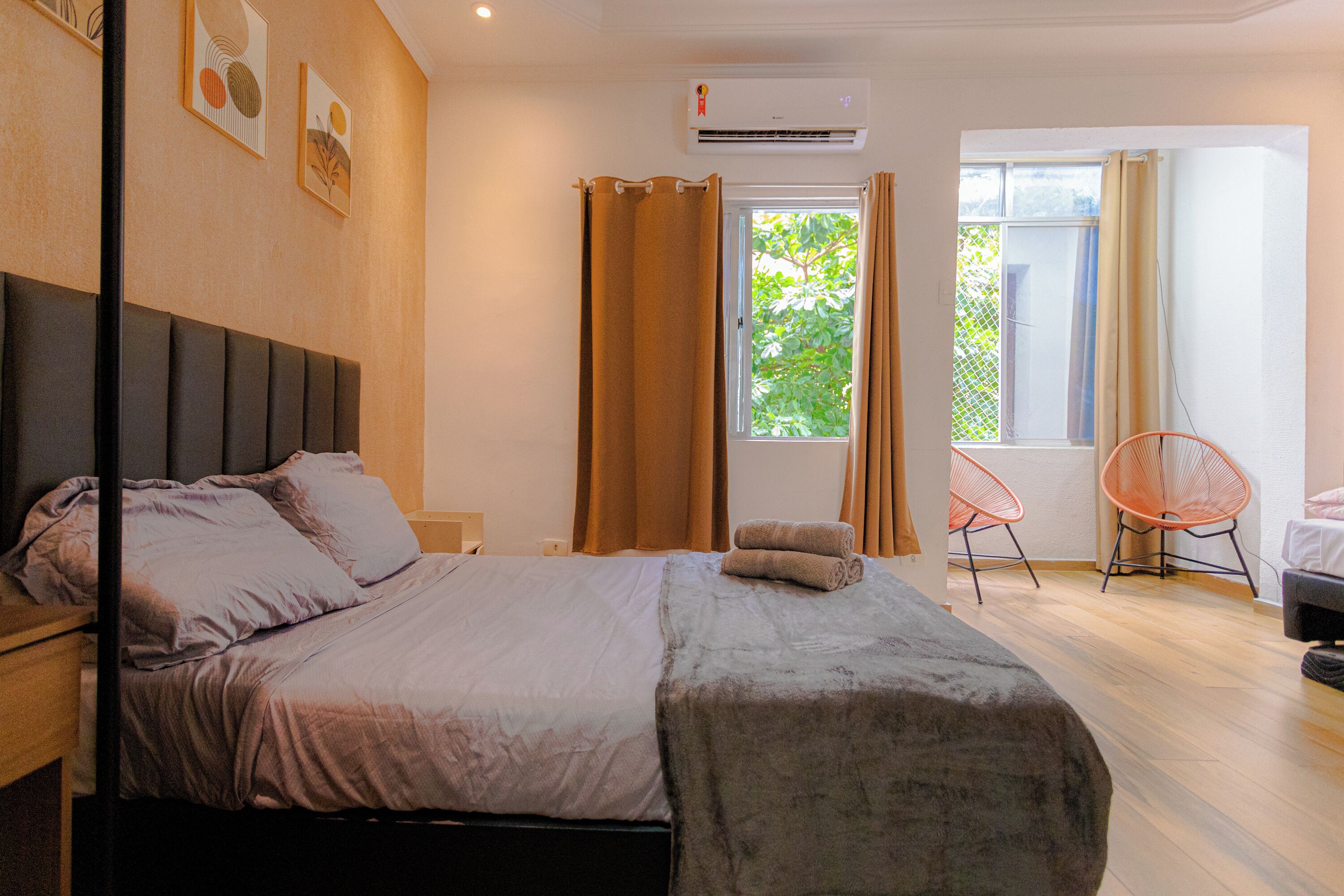 Un dormitorio con cama, cortinas en la ventana, una silla y un equipo de aire acondicionado.