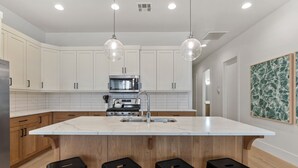 Una cucina moderna con mobili bianchi, un'isola in marmo, sgabelli neri e illuminazione a sospensione.