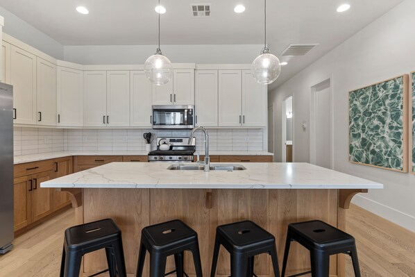 A modern kitchen with white cabinets, a marble island, black stools, and pendant lighting. - Villa #12 at Bloomington Country Club: Pool, Golf, Restaurant (St. George)
