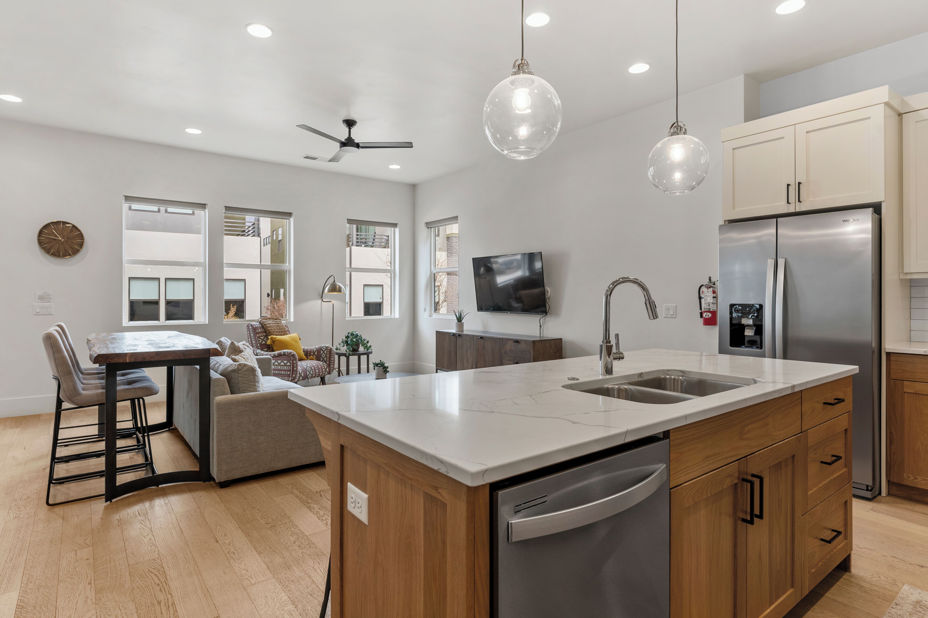 A modern kitchen with a large island, stainless steel appliances, wooden cabinets, and pendant lighting.