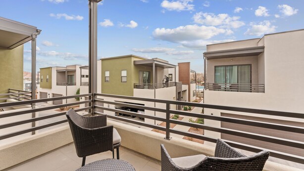 Een balkon met rieten meubels, uitzicht op moderne gebouwen en een heldere lucht.