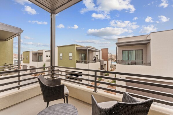 A balcony with wicker furniture, a view of modern buildings, and a clear sky. - Villa #12 at Bloomington Country Club: Pool, Golf, Restaurant (St. George)