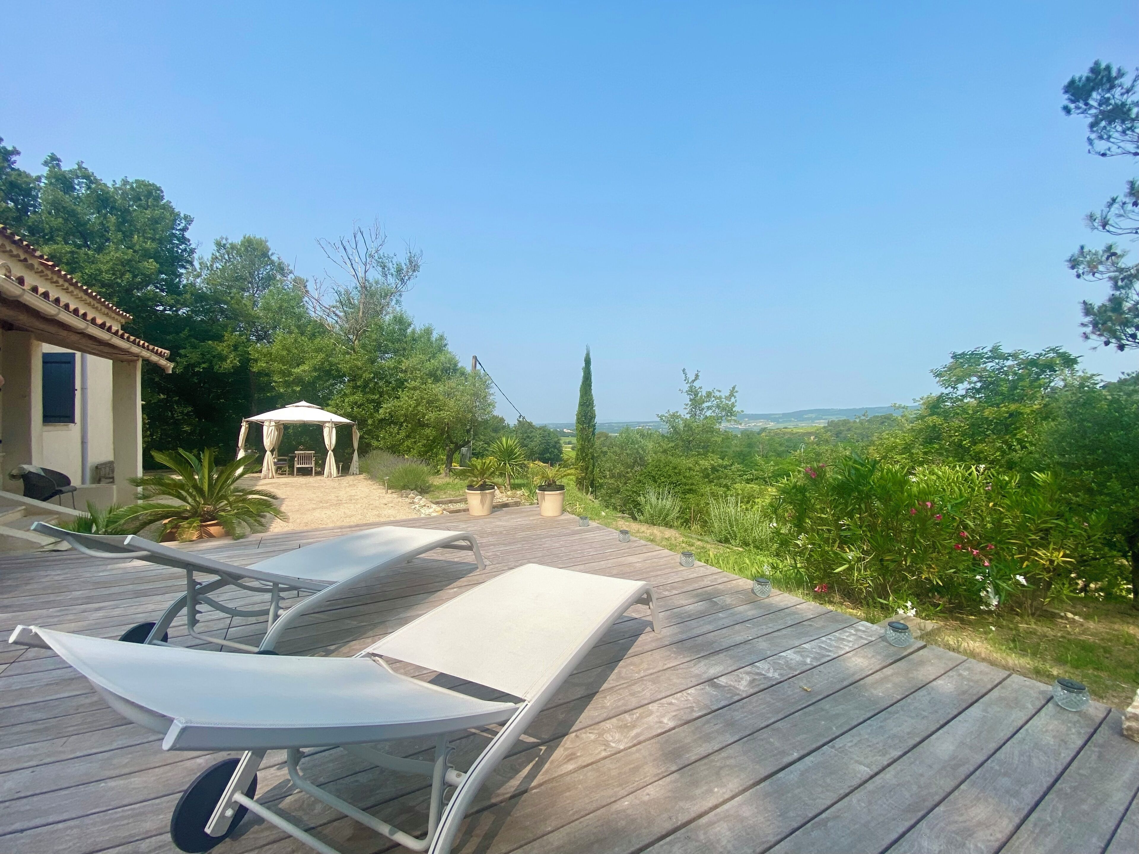 Una terraza de madera con sillones, un pequeño pabellón y vistas a un paisaje exuberante.