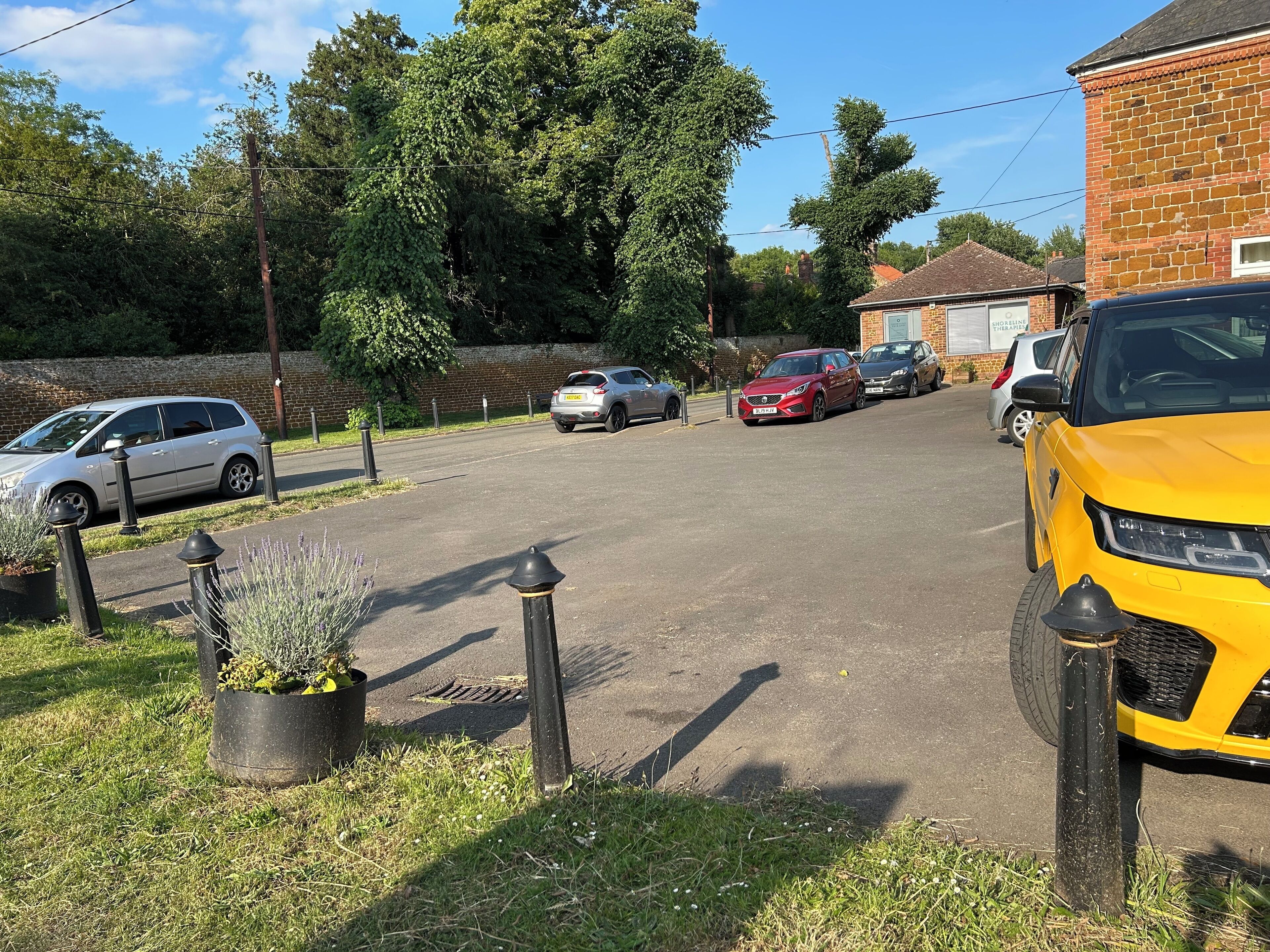 A parking area with multiple cars, a brick building, and a grassy area with potted plants.