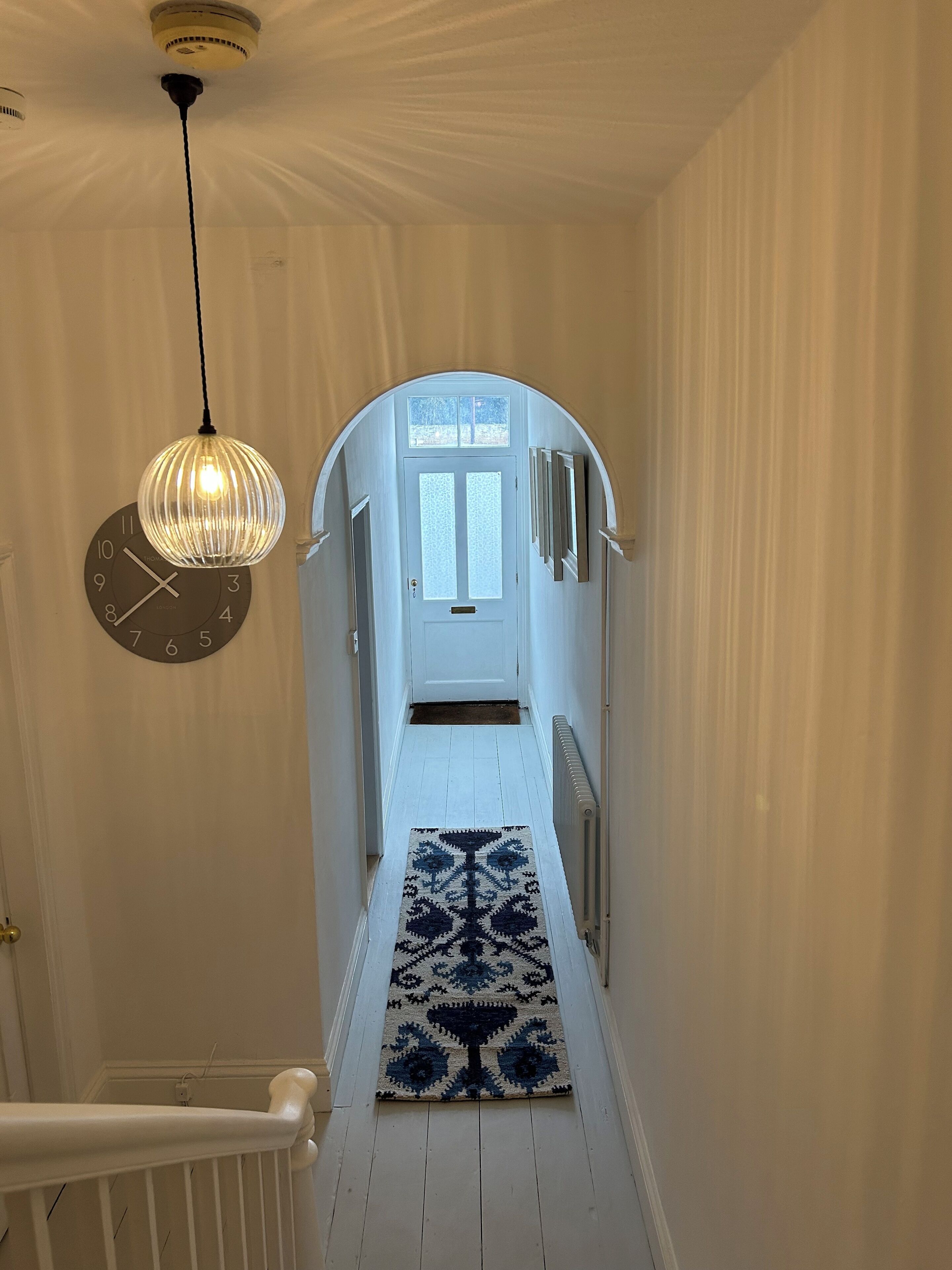 A hallway with a white door, a clock, and a patterned rug.