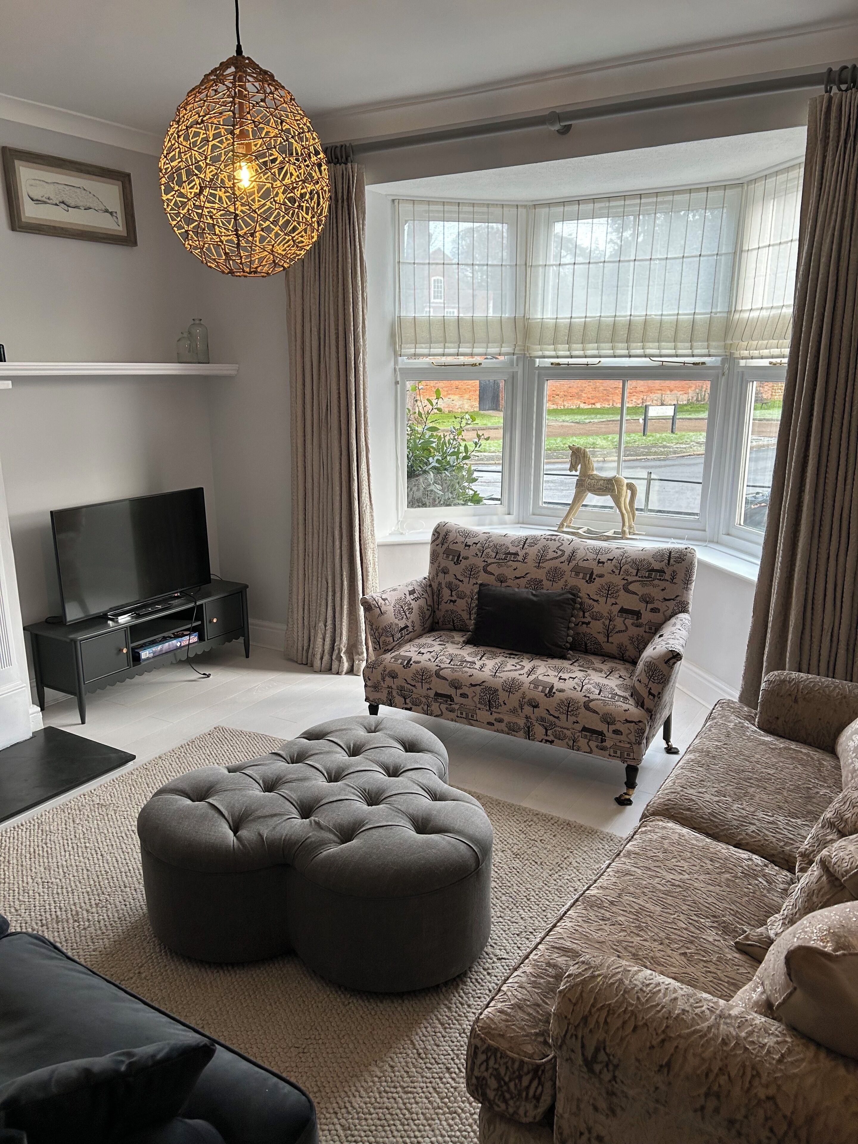 A living room with a sofa, ottoman, TV, and a decorative hanging light.