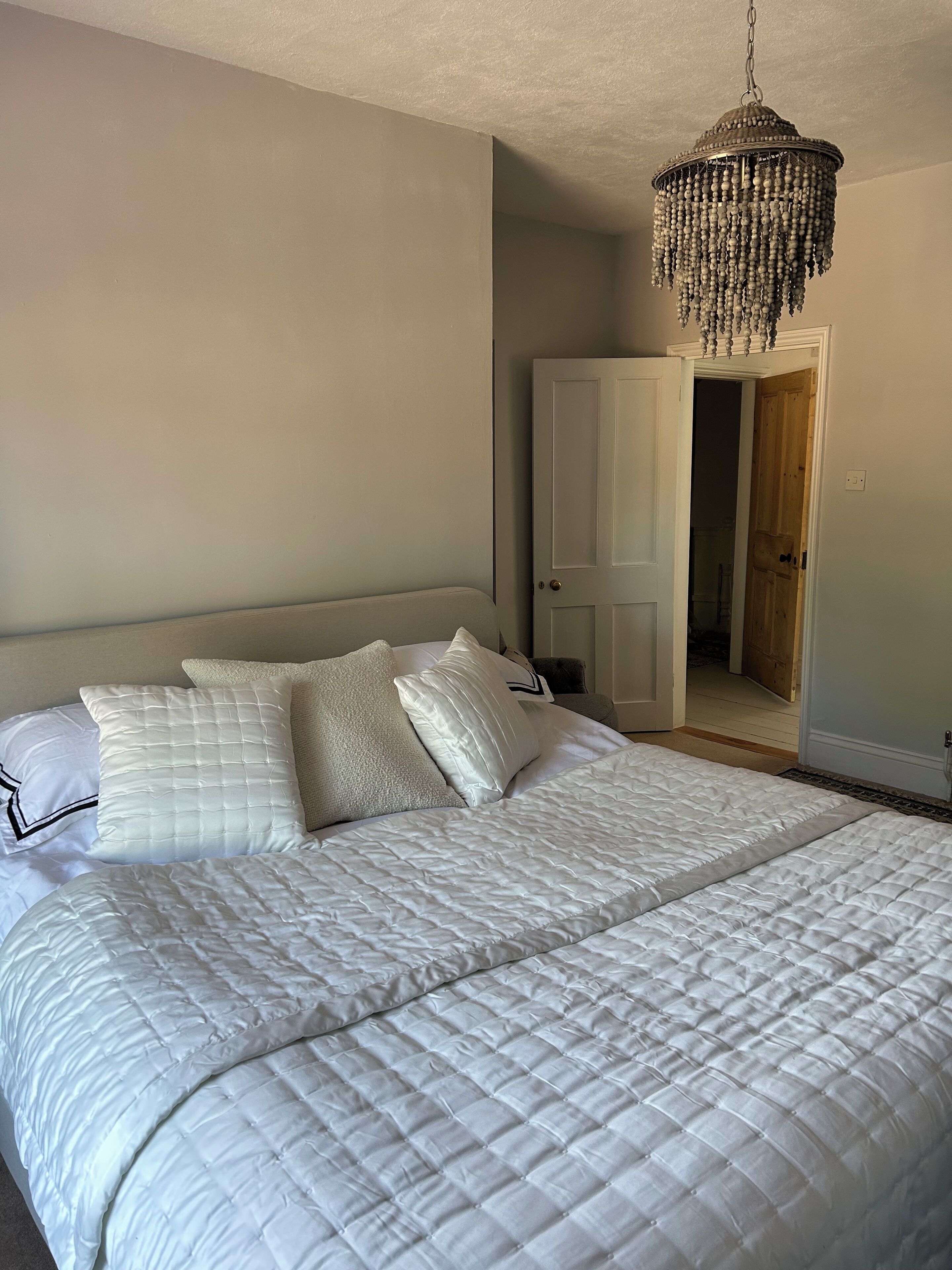 A bedroom with a large bed, a hanging chandelier, and a door leading to another room.