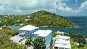 A coastal property with a large building, a dock with boats, and a lush green hill in the background. - Experience the exquisite Mango Serenity, a spacious condo that offers breathtaking views and an abundance of comfort.  Discover your perfect getaway today! (St John)