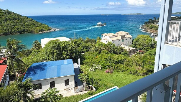 A coastal view with a boat, buildings, and lush greenery. - Experience the exquisite Mango Serenity, a spacious condo that offers breathtaking views and an abundance of comfort.  Discover your perfect getaway today! (St John)