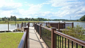 Una terrazza in legno con ringhiere metalliche che si affaccia su un lago, con un'area verde e alberi sullo sfondo.
