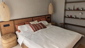 A neatly made bed with white linens and a striped pillow, a woven headboard, and two woven wall hangings.