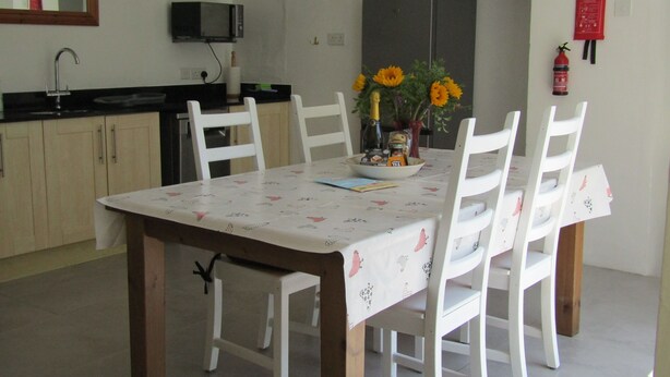 En matplats med ett bord dukat för fyra personer, vita stolar, en vit duk, en vas med blommor och en mikrovågsugn ovanför diskbänken.