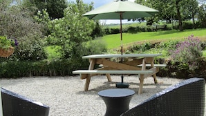 En uteplats med ett träbord för picknick, ett runt bord och stolar av rotting.