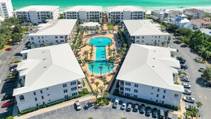 A resort with a central pool surrounded by multiple buildings, a parking area, and a view of the ocean. - Adagio G-403 Poolside 3/3 - NEW to program for 2025! (Santa Rosa Beach)