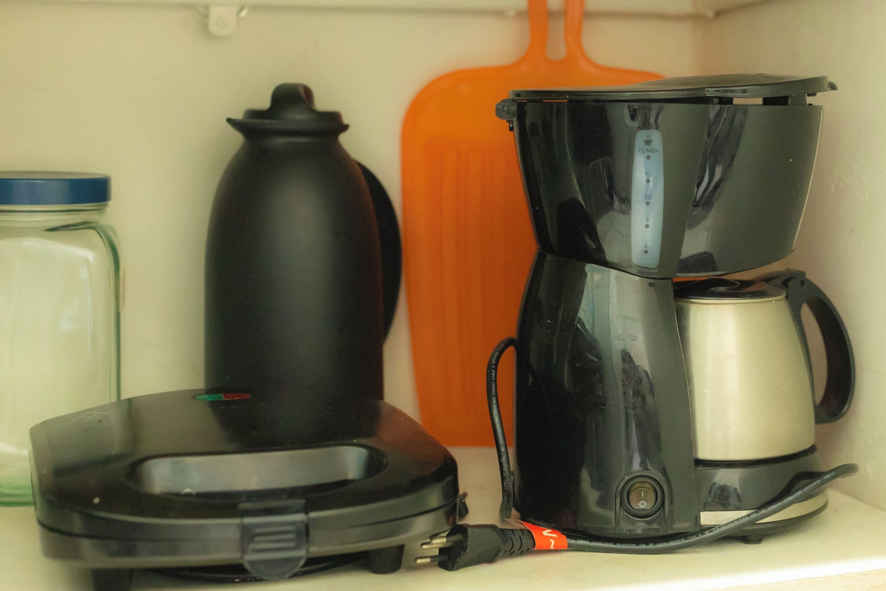 A kitchen shelf with a coffee maker, a kettle, and a container.