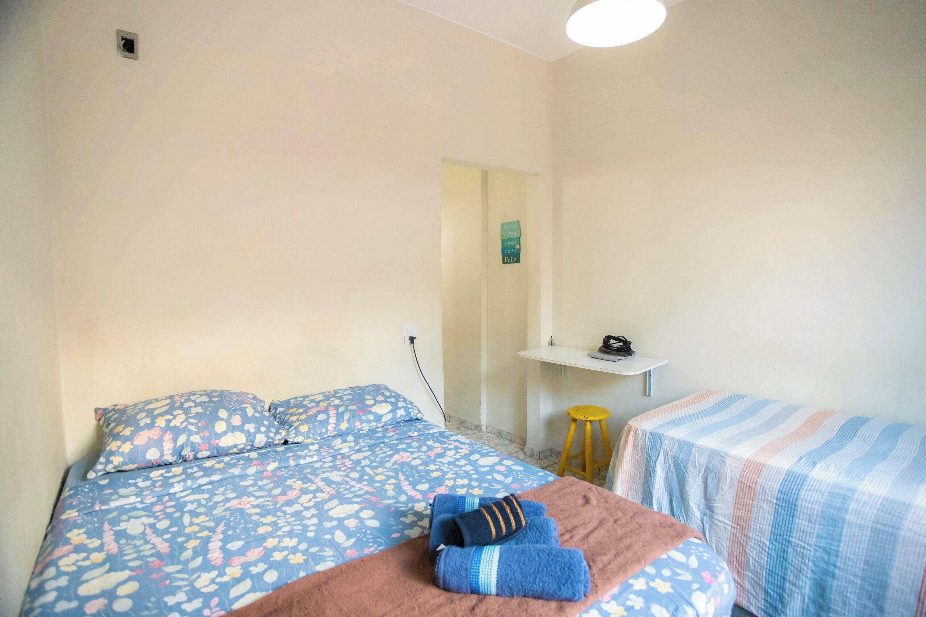 A bedroom with a bed, a small desk, and a stool.