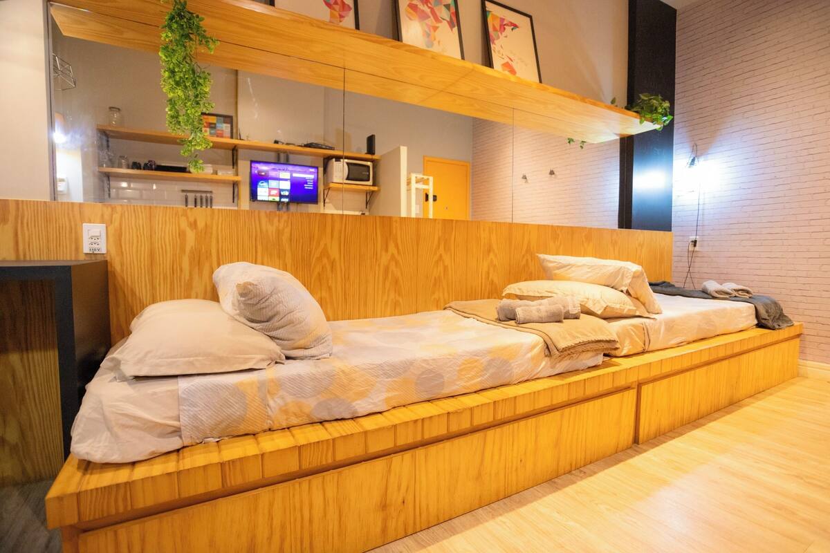 A modern room with a wooden bed, built-in storage, a television, and a brick wall.