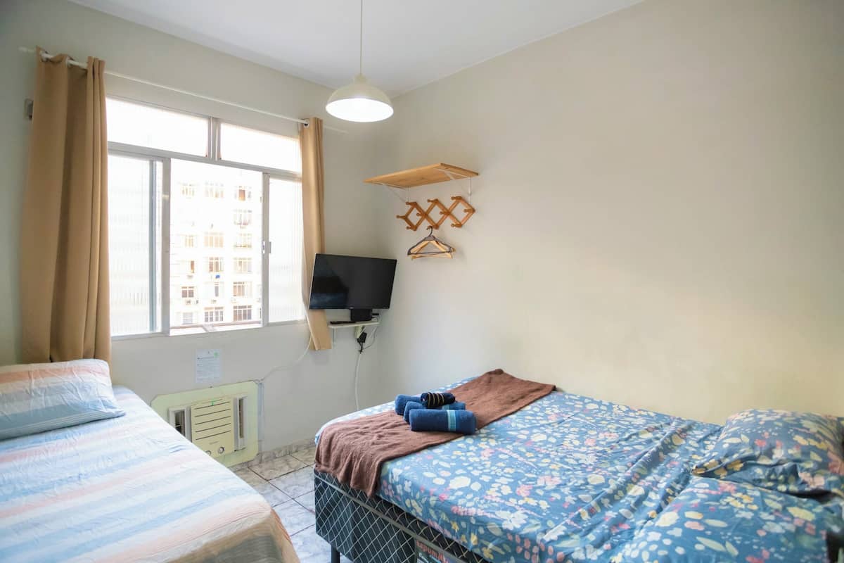 A bedroom with a bed, a TV, a window, and a radiator.