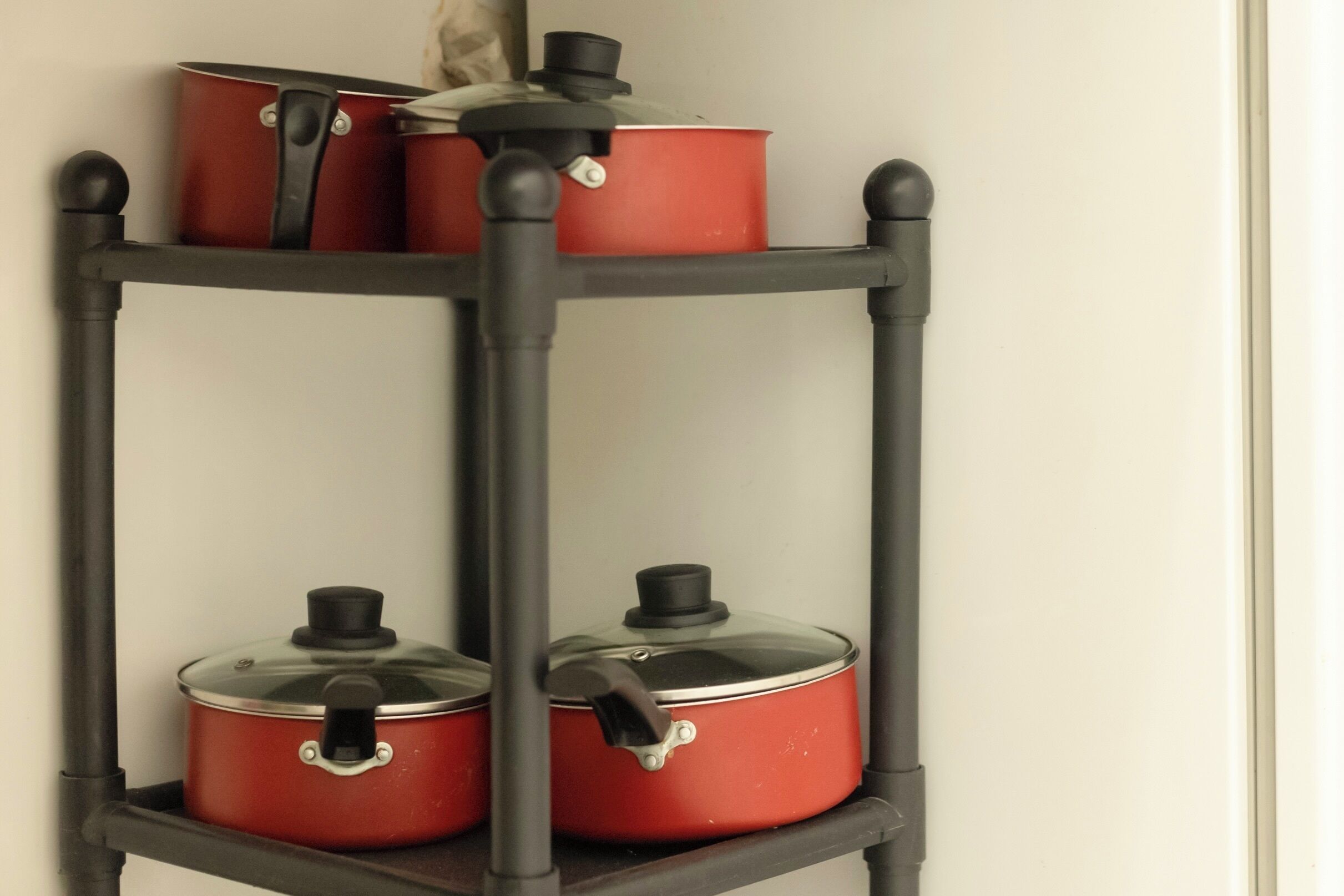 Una mensola in metallo nero con tre pentole rosse, complete di coperchi fissati da un fermaglio nero.