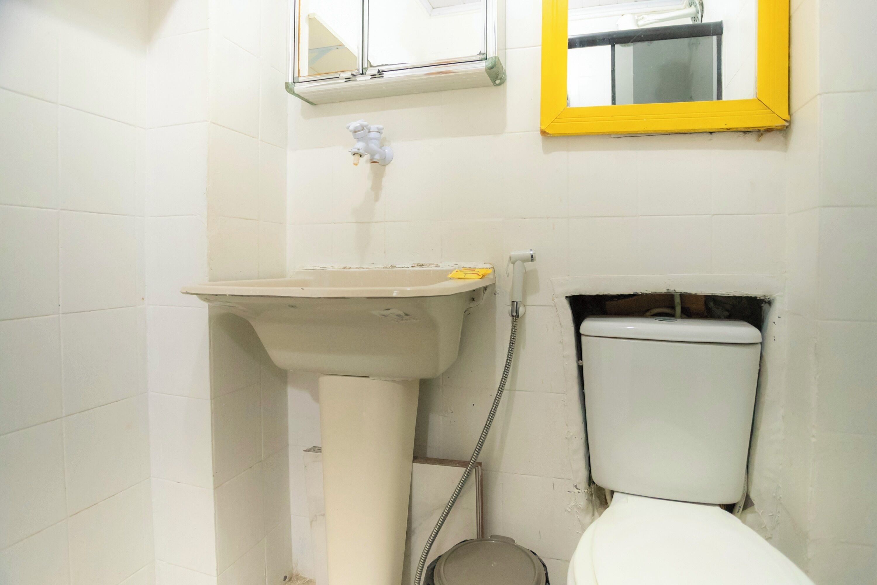 Een badkamer met een witte wasbak, een spiegel met een geel kader, en een wit toilet.