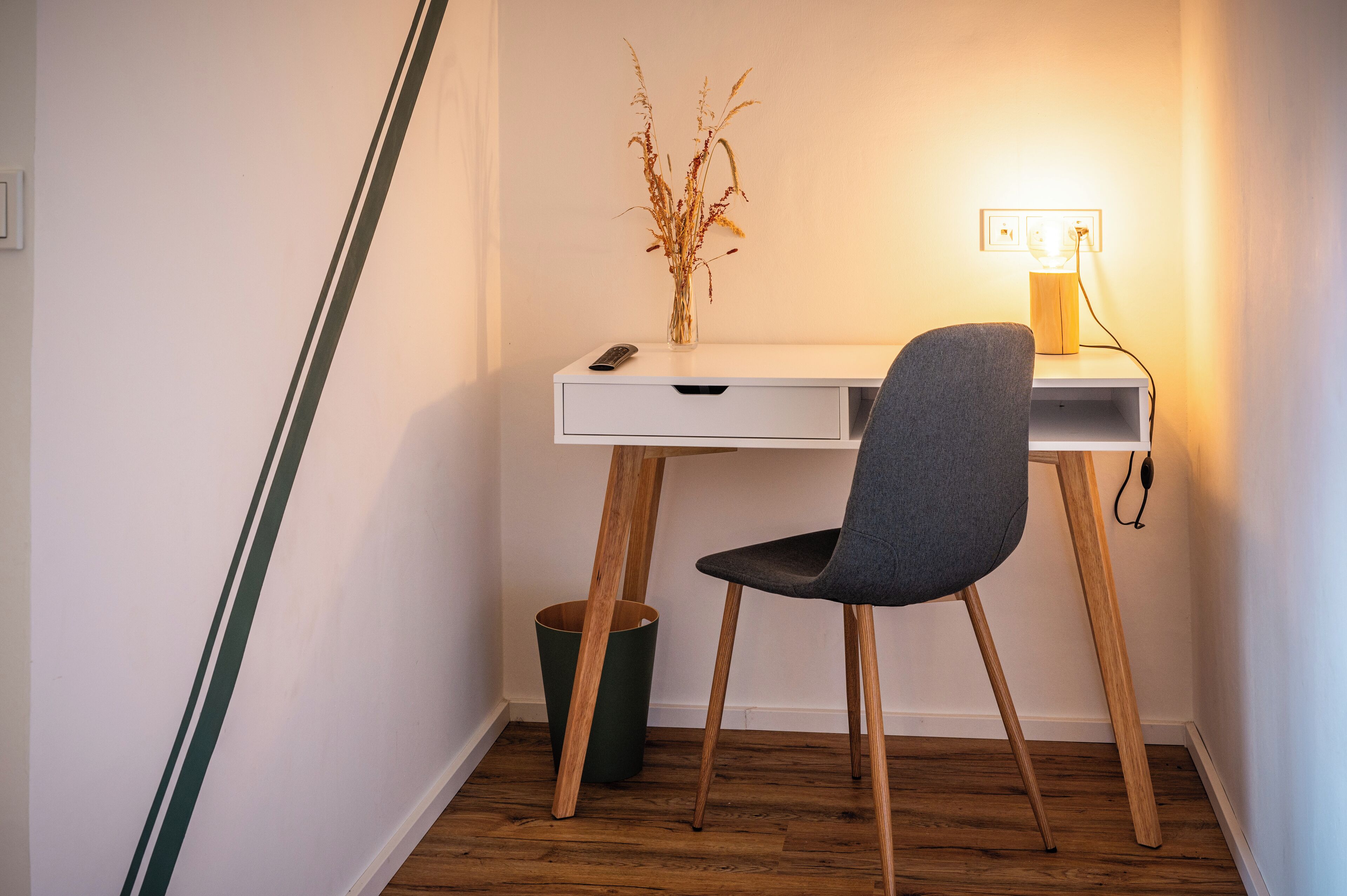 Un escritorio con una silla, un jarrón con plantas secas y una lámpara.