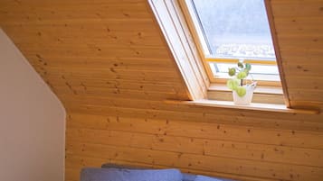 Un dormitorio tipo loft con techo inclinado, un sofá gris y un ventanal con una planta.