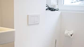 Ein modernes Badezimmer mit Toilette, einem Handtrockner, einem Mülleimer und einem Fenster mit Blick auf Bäume.
