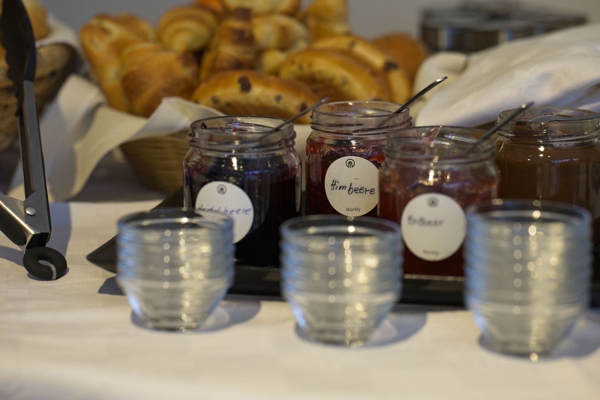 Una mesa con frascos de mermelada y una cesta de cruasanes.